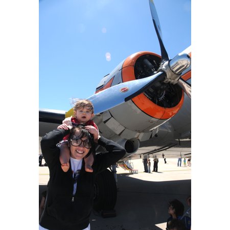 0689762100212 - LAMINATED POSTER MARIAUL WAVRA HOLDS HER COUSIN JOSEPH ON HER SHOULDERS SO HE CAN SEE THE PLANES AS THEY FLY BY DURIN POSTER PRINT 24 X 36